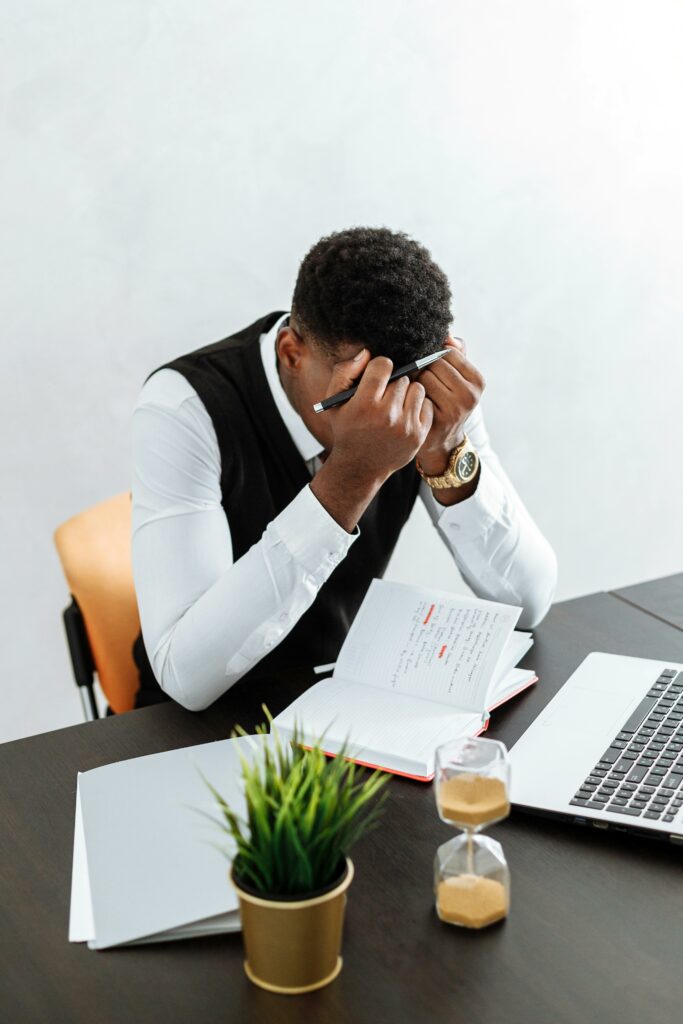 pexels-photo-5060985-5060985 A businessman overwhelmed working indoors with a notebook, laptop, and hourglass.